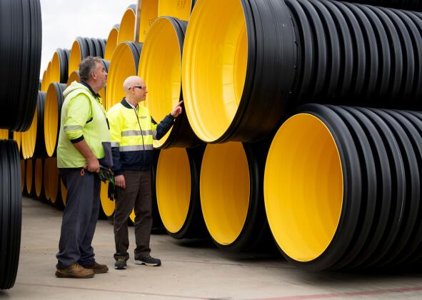 BlackMax large‑diameter corrugated polyethylene drainage pipes stacked at the Iplex Albury distribution yard, showing yellow interior and pipe openings.