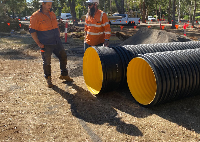 Two construction workers in high-visibility clothing standing beside large Iplex BlackMax corrugated drainage pipes at a Keystone Civil construction site