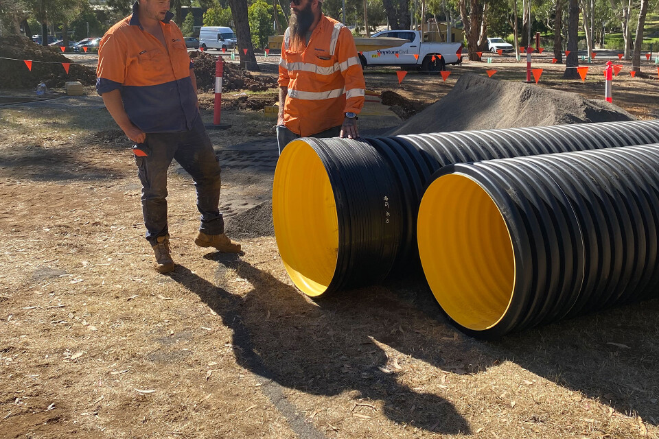 Two construction workers in high-visibility clothing standing beside large Iplex BlackMax corrugated drainage pipes at a Keystone Civil construction site